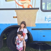 Two girls stand infront of the Bookmobile wheel in Bayfront Park